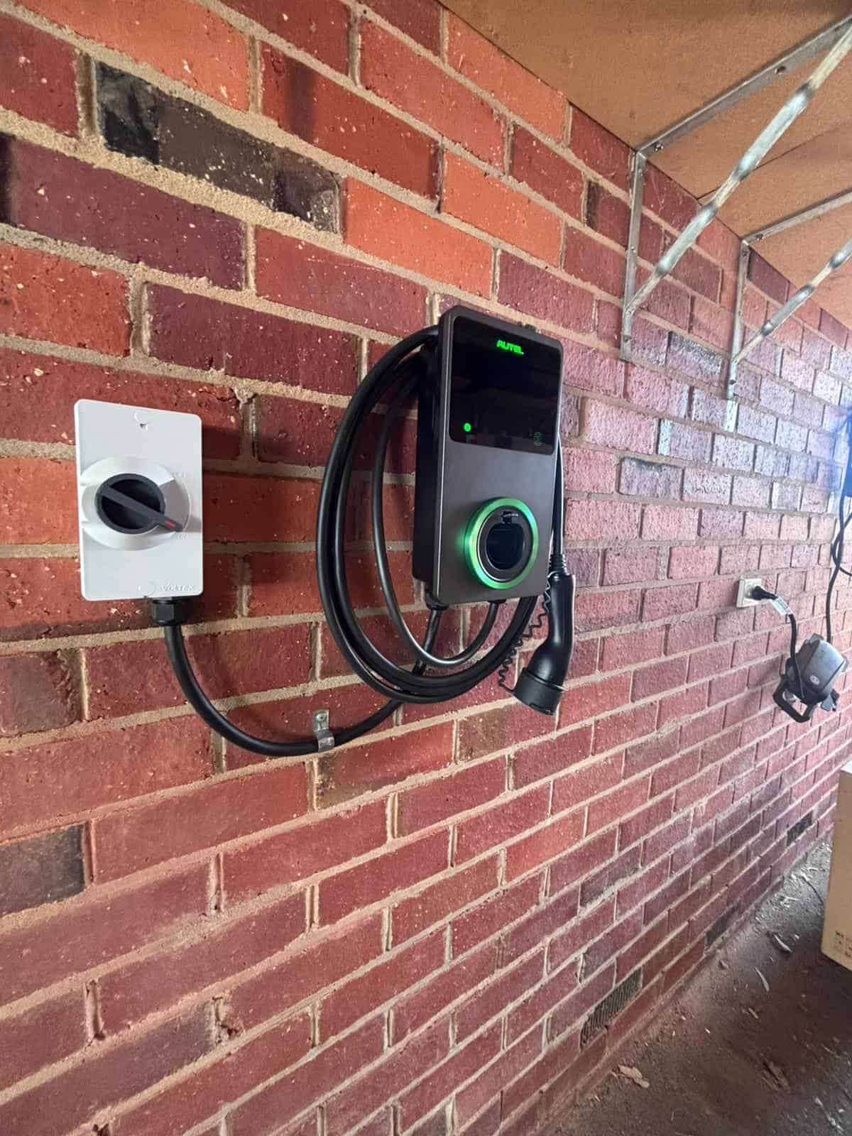 EV charging station mounted on a brick wall, connected to a power outlet inside.