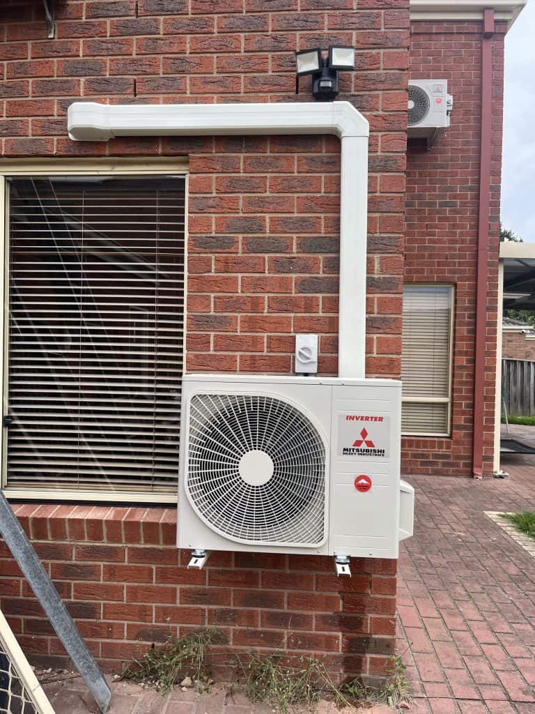 Air conditioning unit installed on exterior brick wall of a building outside.