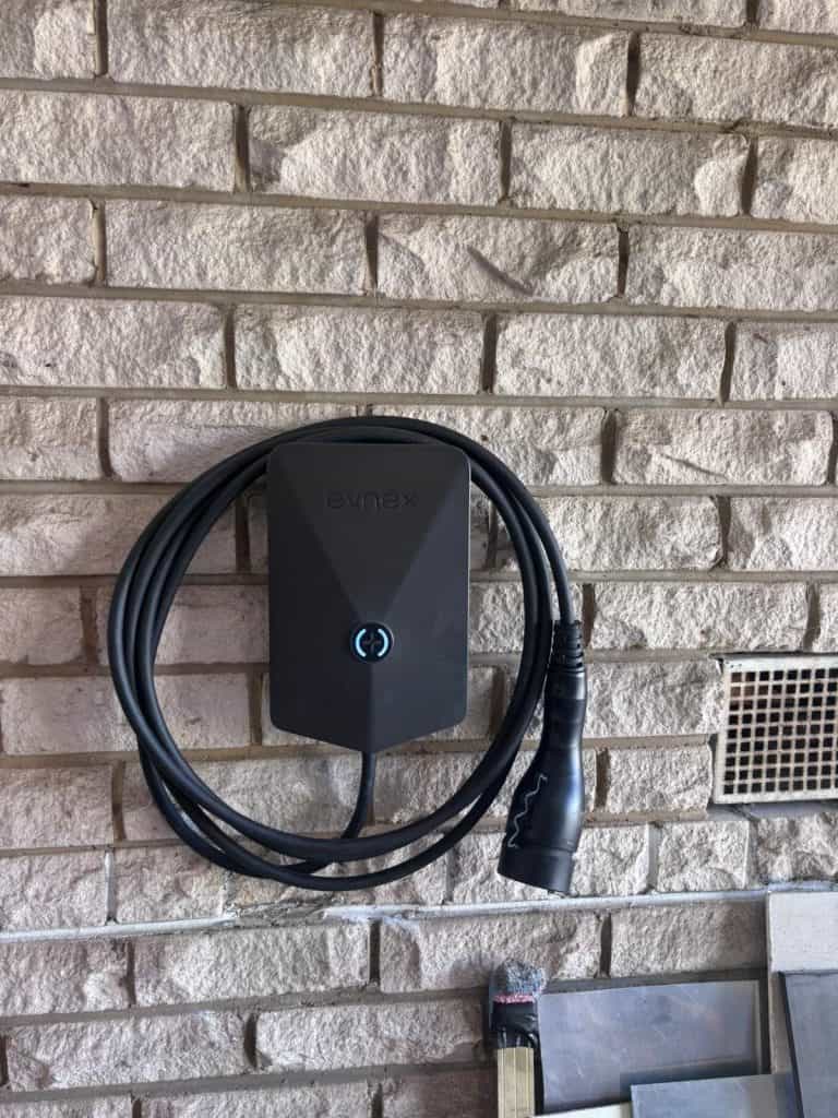 EV charging station mounted on a beige brick wall outside.