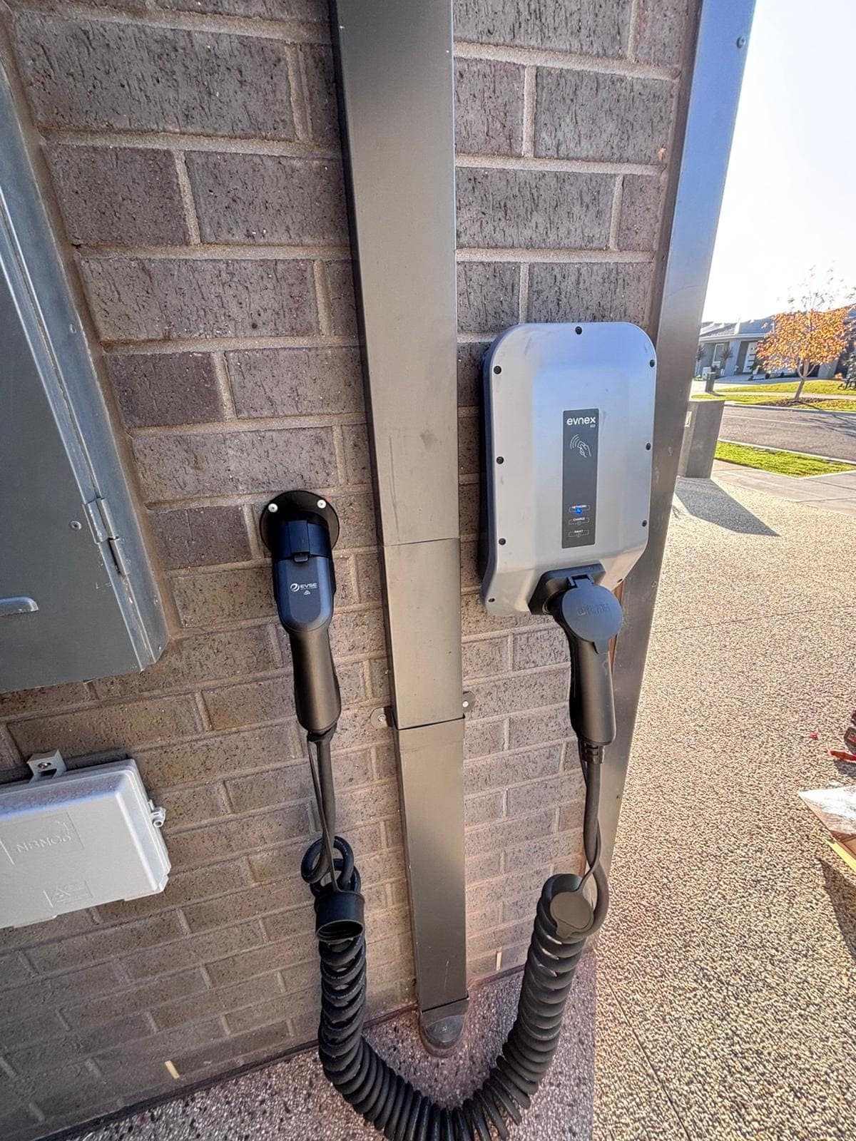 EV charging station outdoors on brick wall, connected with power cables.