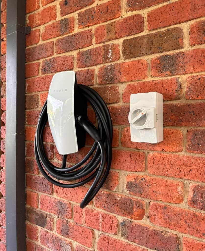 Electric vehicle charging station mounted on an outdoor red brick wall.