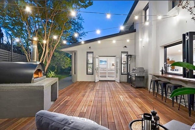 Outdoor wooden deck with string lights and a built-in fire oven on the patio.