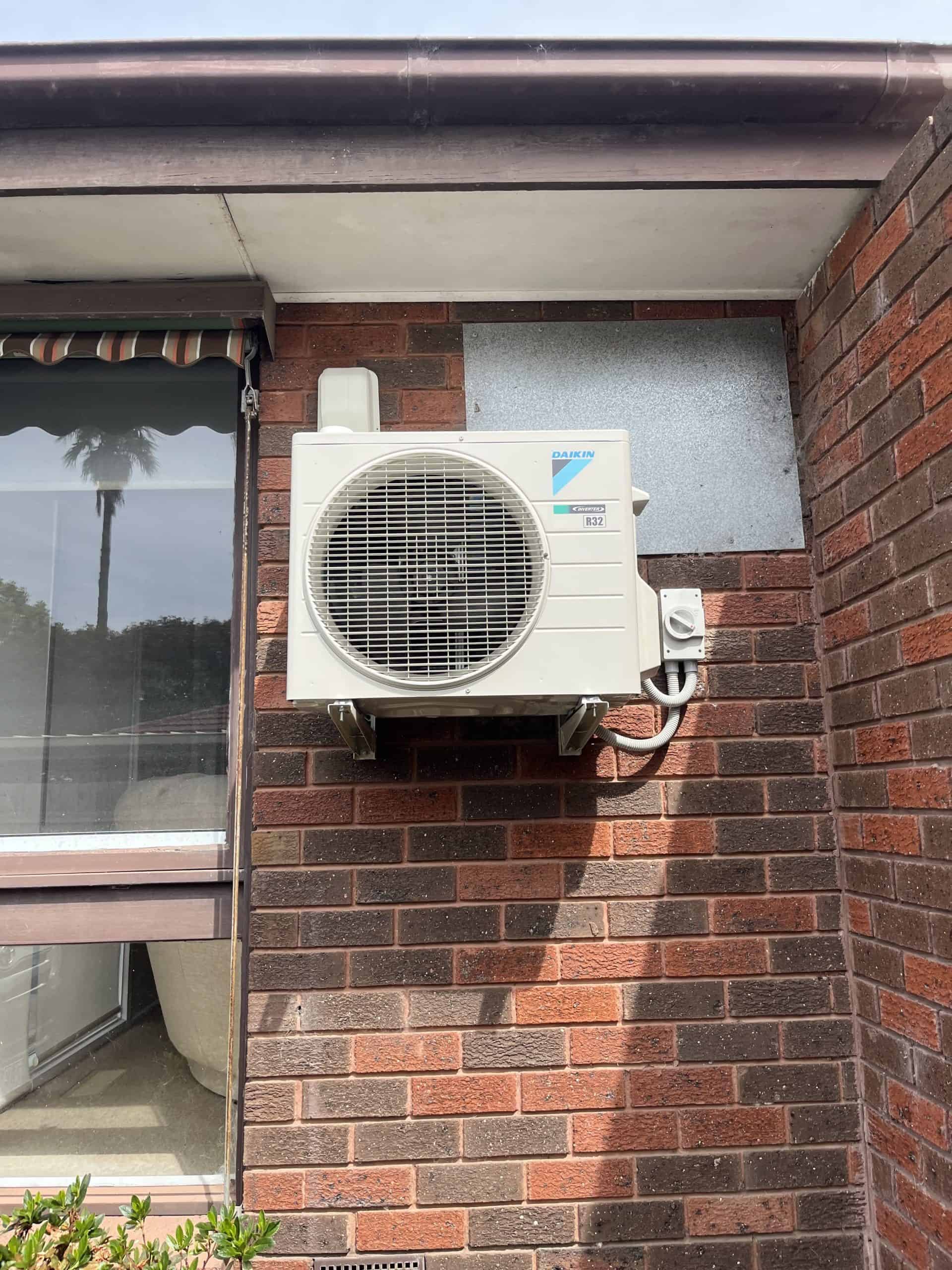 AX4 air conditioning outdoor unit mounted on red brick wall outside building.