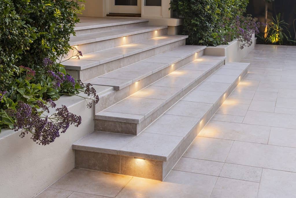 Modern outdoor stairway illuminated by embedded step lights on a tiled porch area.